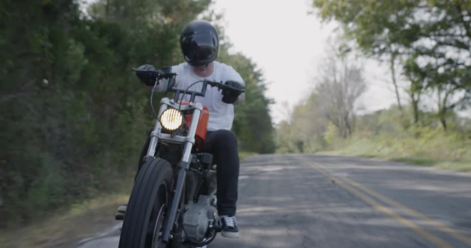 Man drives a motorcycle on a tree lined country road
