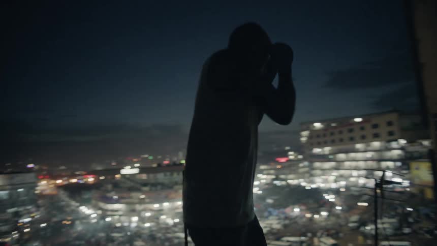 A boxer punches the air in a city at night