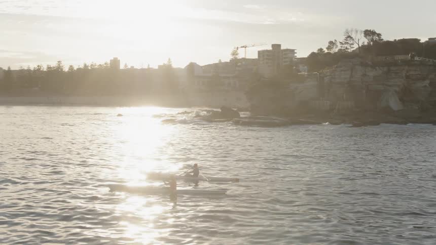 People kayak just off the coast at sunset
