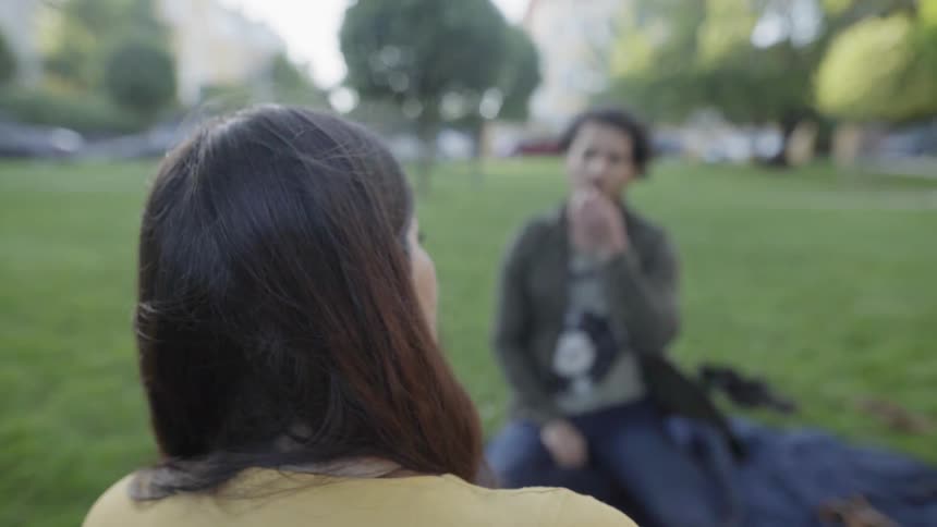 A man and woman are talking as they picnic outside in a park