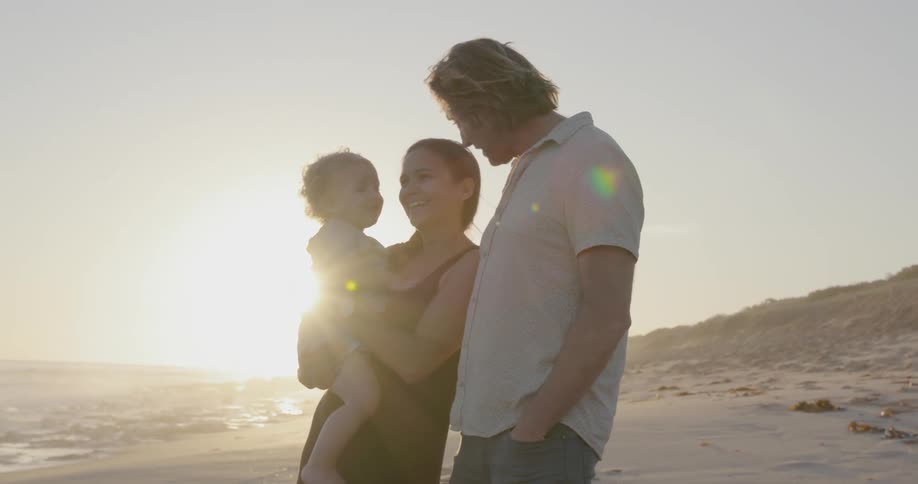 A young family stands on a beach at sunset