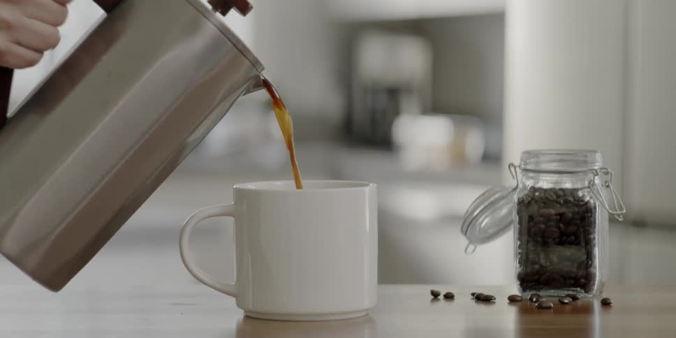 Person pours coffee into a mug out of a silver pitcher