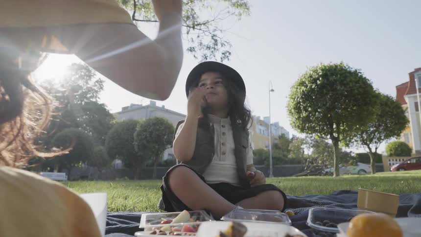 A young child sitting on a blanket playing with mother during park picnic.