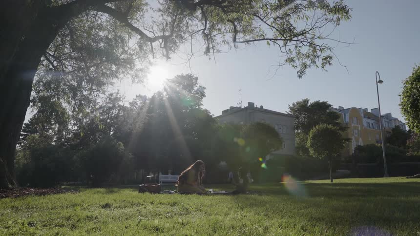wide shot of mother and child sitting on blanket during park picnic.