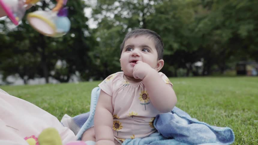 A girl and baby sit on a blanket on a lawn