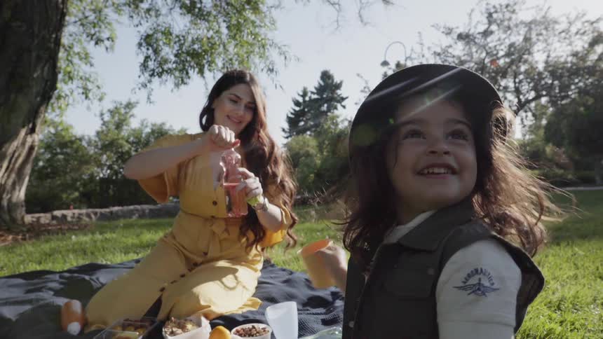 A young mother opening juice bottle while child smiles happily at picnic.