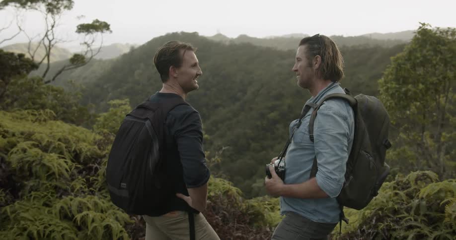 Two men stand on tree covered hills talking