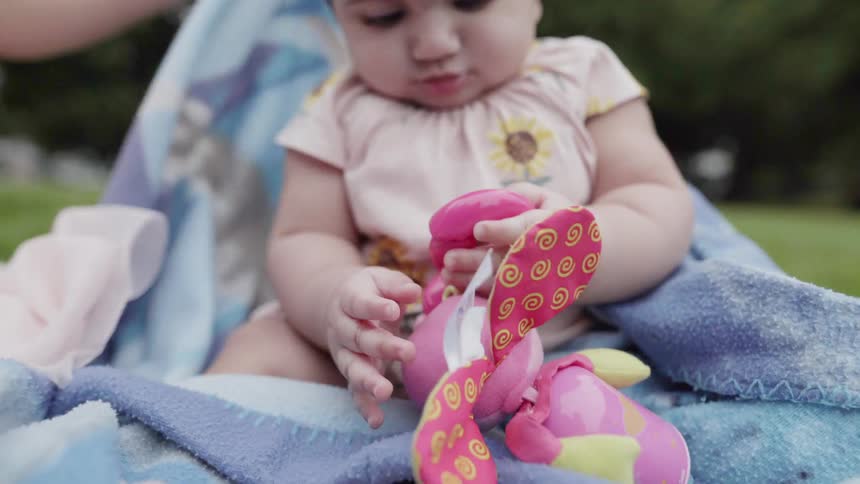 Baby on blanket in park plays with toy