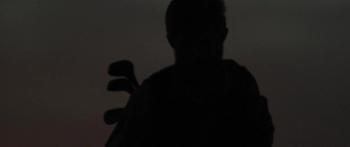 The silhouette of a golfer carrying clubs at sunset