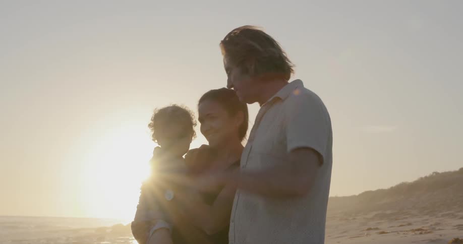 A young family stands on a beach at sunset