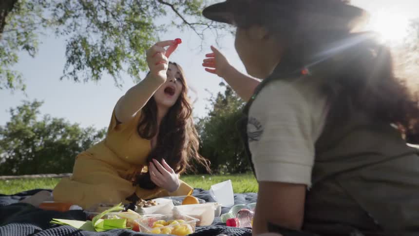 A mother feeding a small piece of fruit to her child outdoors.