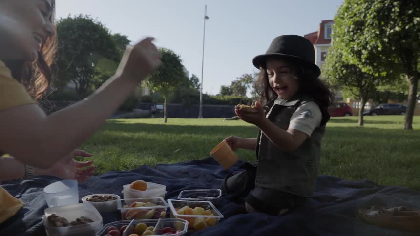 A young boy wearing a hat laughing playfully during an outdoor picnic.