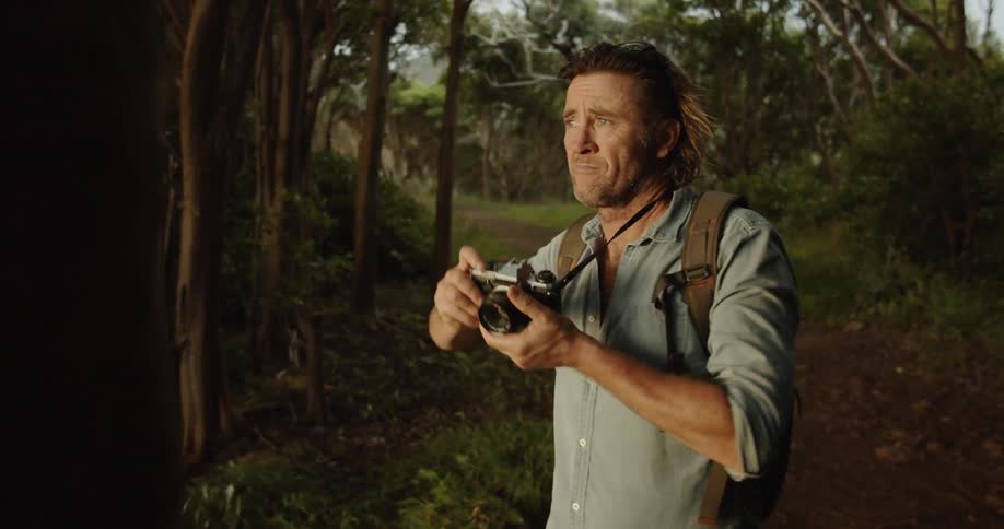 Man stands in the woods taking a picture with a camera