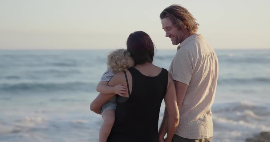 A young family stands on a beach at sunset