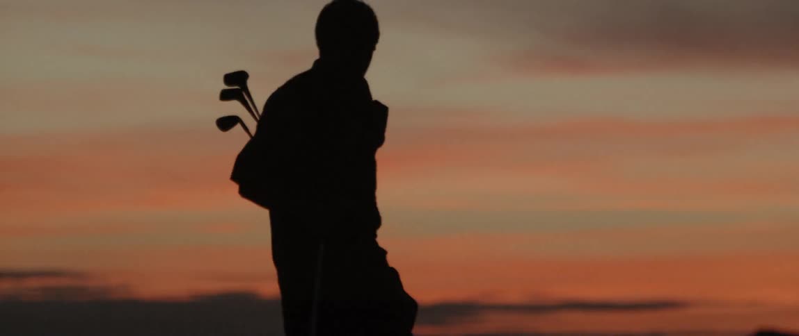 Man walks as he carries a bag of golf clubs