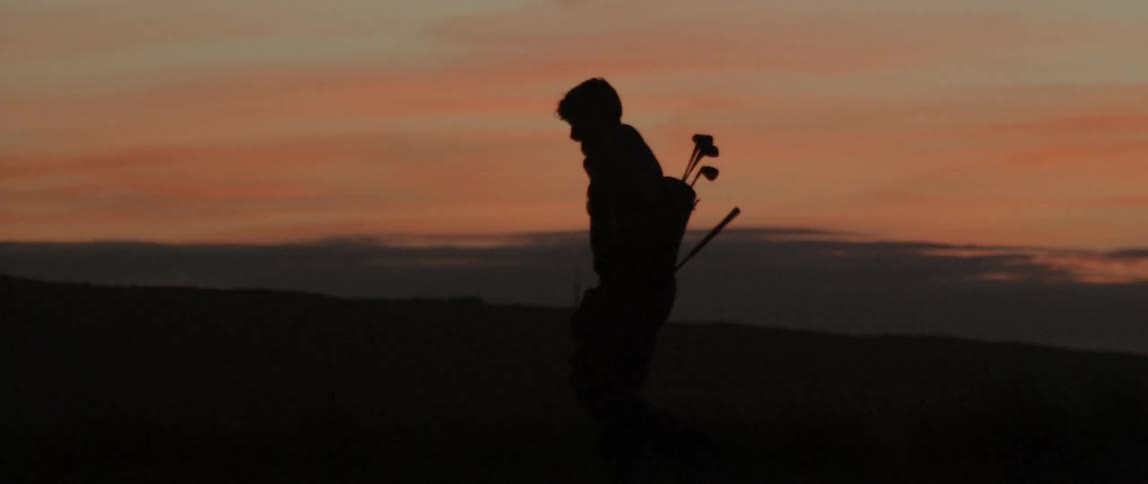 Man carrying golf clubs is walking outside after sunset