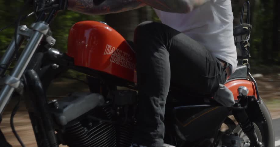 A tattooed man motorcycles on a rural road
