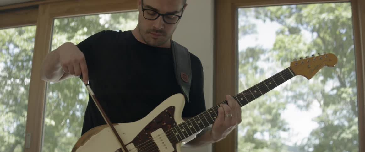 A man plays an electric guitar with a bow