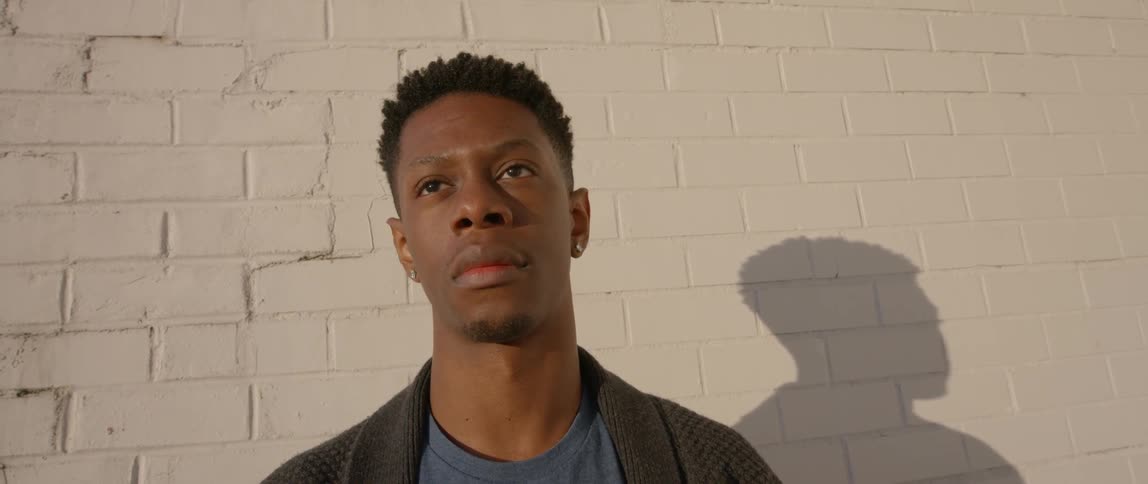 A man stands in front of a brick wall