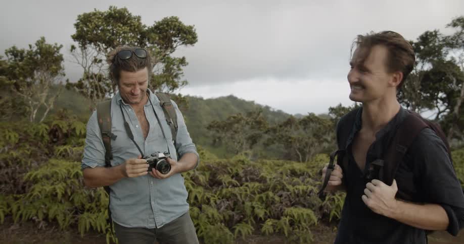 Man takes a picture of a man while they stand on hilly tree covered landscape