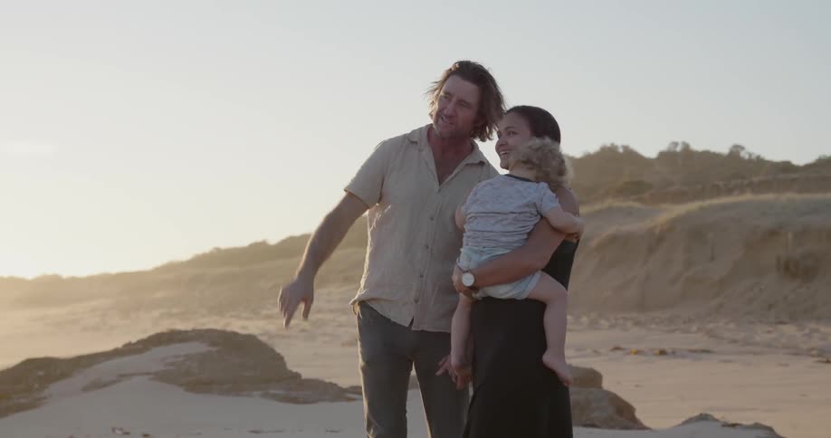 A young family stands on a beach at sunset