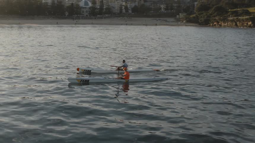 Two men kayak just off the coast at sunset