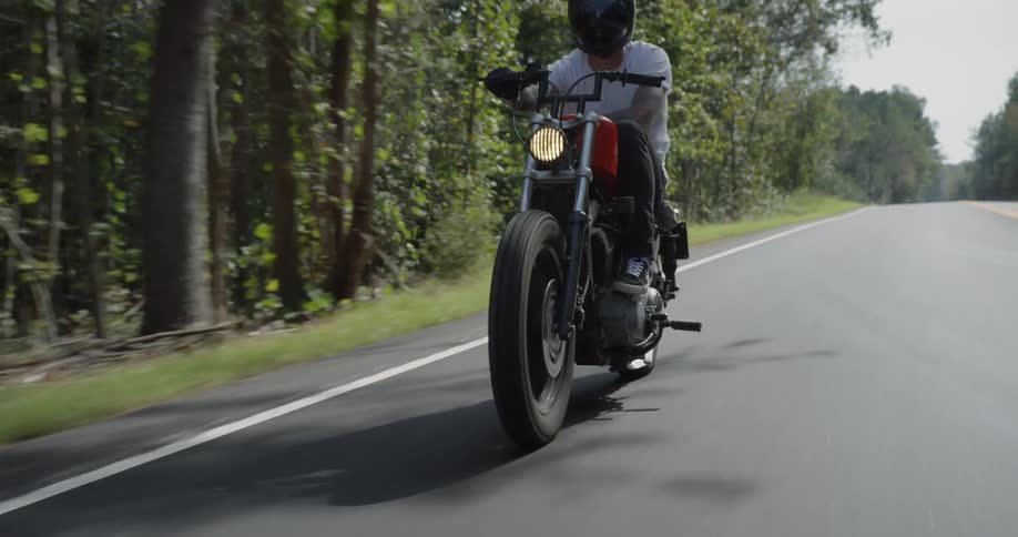 A man rides a motorcycle on a rural woodsy road