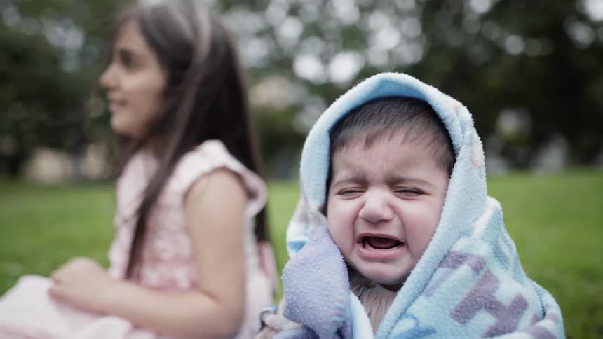 Two children in blankets sitting on the ground