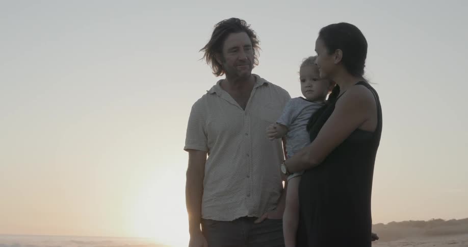 Man talks to a woman who is holding a child while standing on the beach