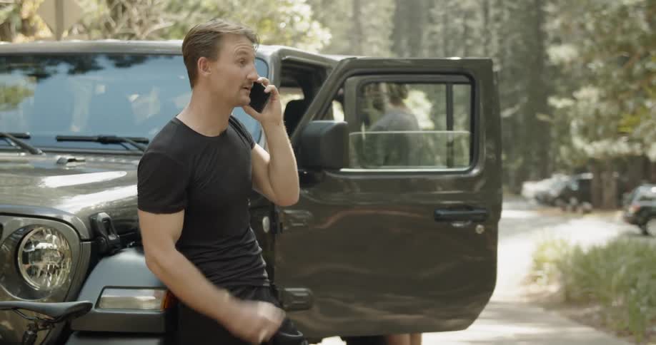 A man talks on the phone next to a parked car