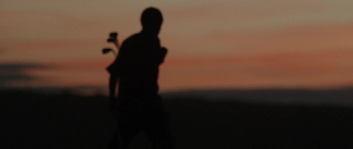 A man carries golf clubs outside