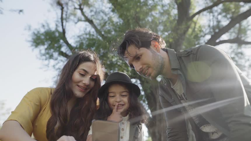 Man, woman and child look at a phone and smile on a sunny day