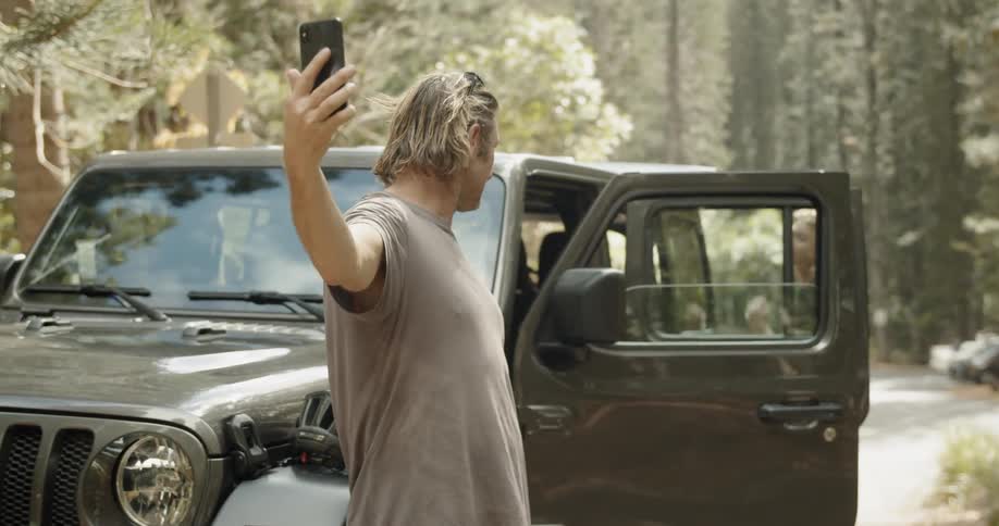 A man makes a video call next to a parked car