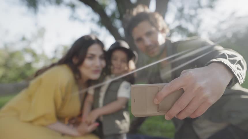 A happy family smiling together taking a selfie picture outdoors on sunny day.