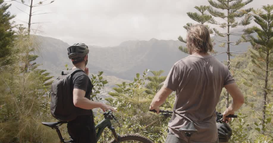 Two men stand near their bikes in the forest