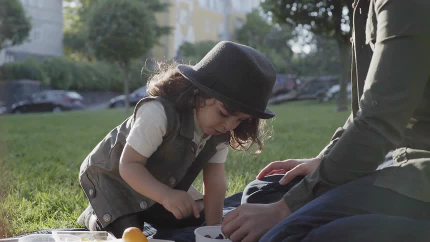 A boy is eating raisins as his father watches outside in a park in daylight