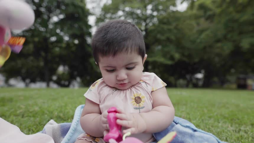 A girl and baby play on a blanket on a lawn