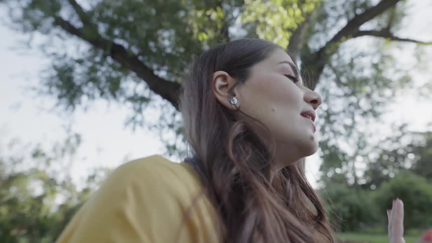 A young woman sitting outdoors in a sunny park talking and smiling happily.