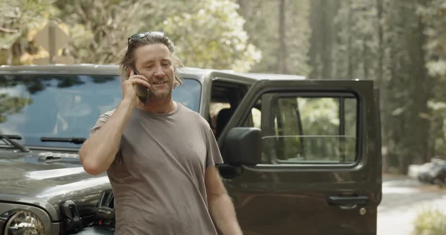 Man is standing outside next to jeep while talking on cell phone