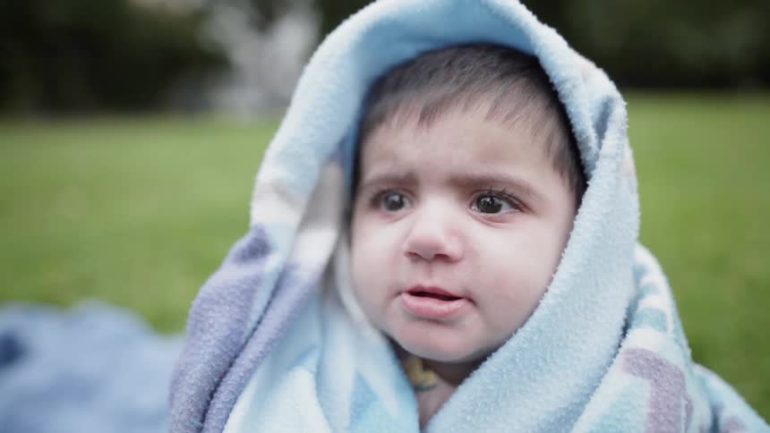 Child sits on grass with blanket around head