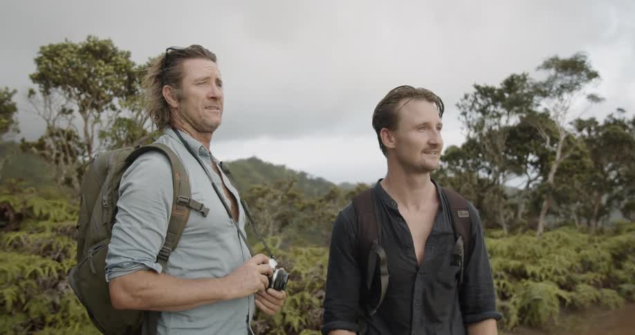 Two men walk on a dirt path looking around at nature