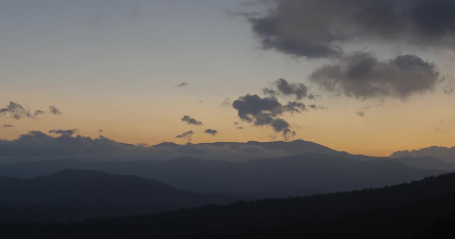 Sun sets behind mountains with puffy clouds overhead