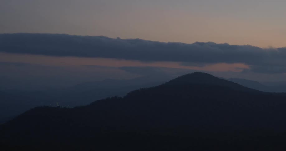 Clouds are hovering on the horizon at dusk above coastal mountains