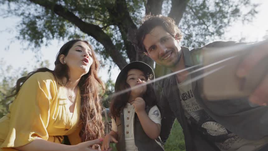 Man takes a picture of himself and a woman and child outside on a sunny day