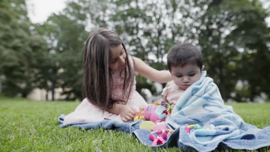 A young girl and baby sit on a blanket on a lawn