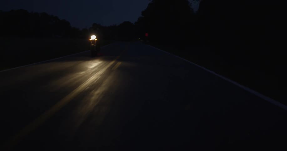 A motorcyclist rides on a rural road at night