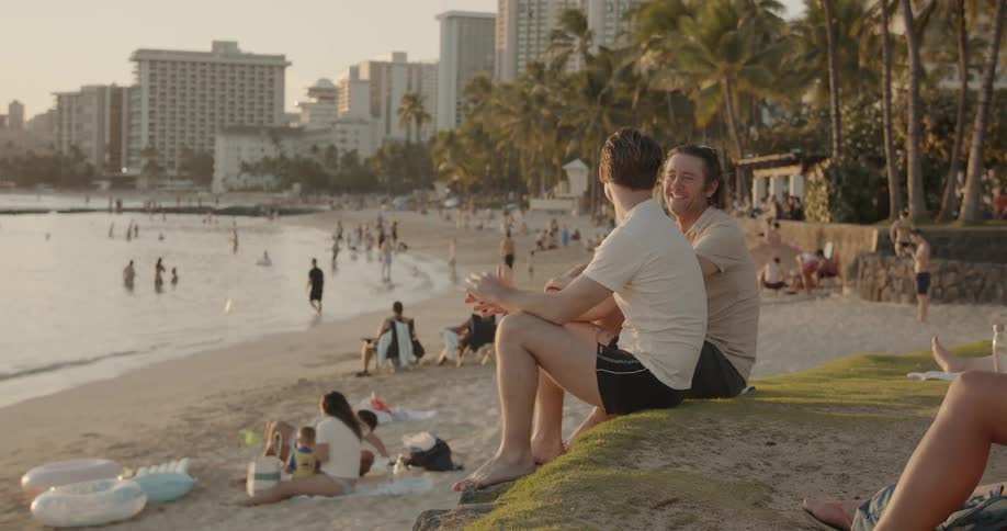 Two men talk on a beach at sunset