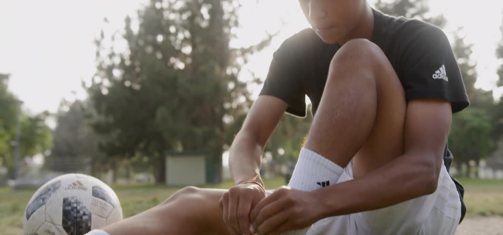 A soccer player ties their shoelace on a soccer field