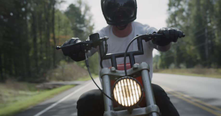 A man motorcycles on a tree-lined road
