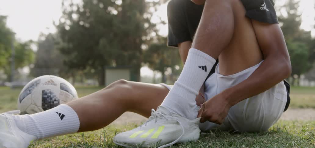 Man sits on the ground as he puts on his soccer shoe